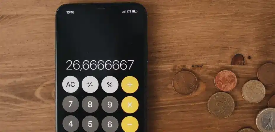 Gros plan d'une calculatrice de smartphone et de pièces de monnaie sur une surface en bois pour une métaphore financière.