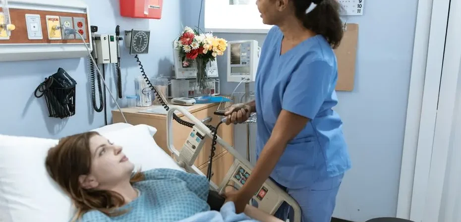 Infirmière prodiguant des soins à un patient dans une chambre d'hôpital avec du matériel médical.
