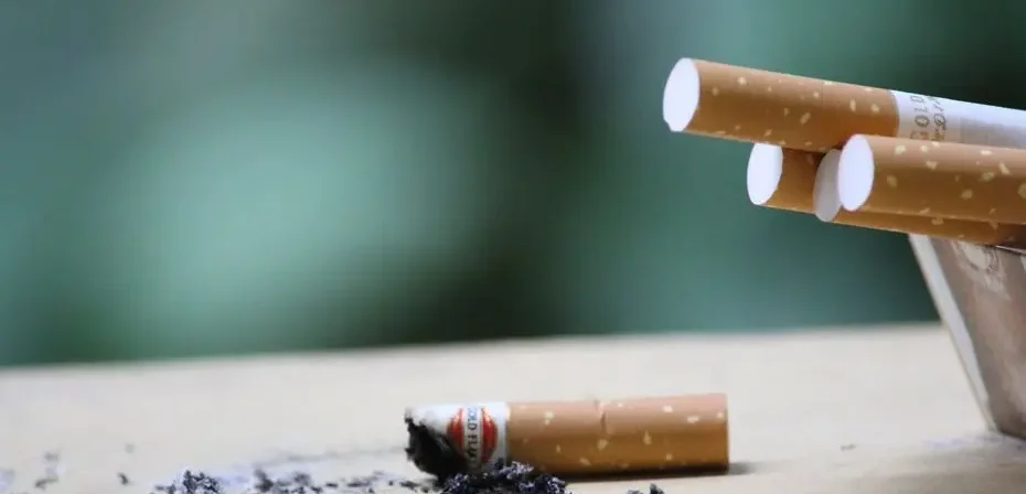 Cigarette avec des cendres sur une surface, mettant en évidence l'usage du tabac et les risques pour la santé.