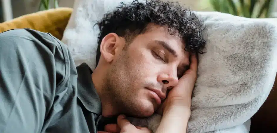 Un jeune homme aux cheveux bouclés dormant paisiblement sur un canapé confortable avec un oreiller doux.