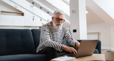 Homme senior avec des lunettes utilisant un ordinateur portable dans un salon moderne et stylé.