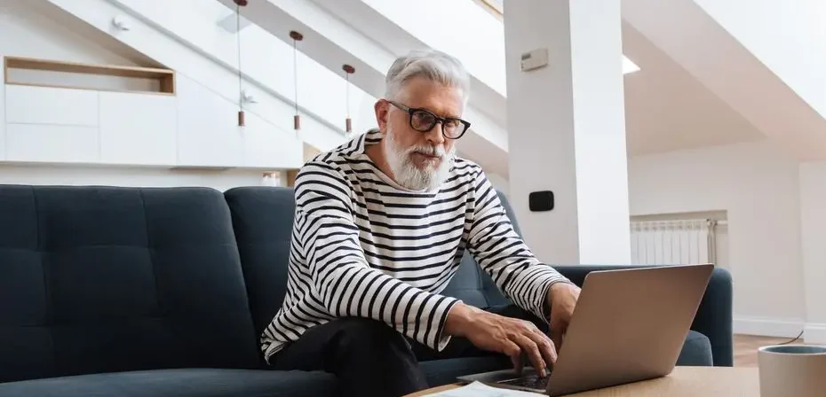 Homme senior avec des lunettes utilisant un ordinateur portable dans un salon moderne et stylé.