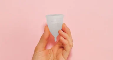 Une main tenant une tasse menstruelle rose sur un arrière-plan rose vif, soulignant la durabilité et la santé féminine.