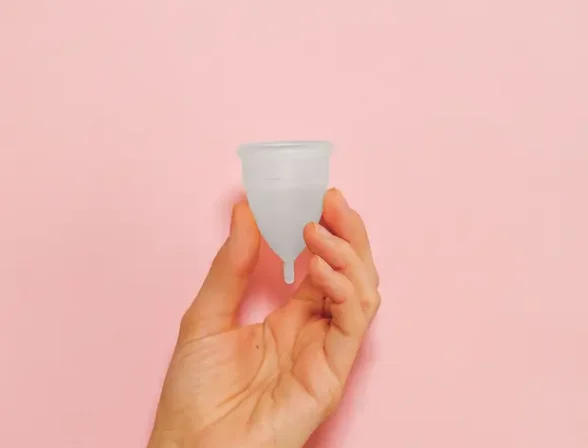 Une main tenant une tasse menstruelle rose sur un arrière-plan rose vif, soulignant la durabilité et la santé féminine.