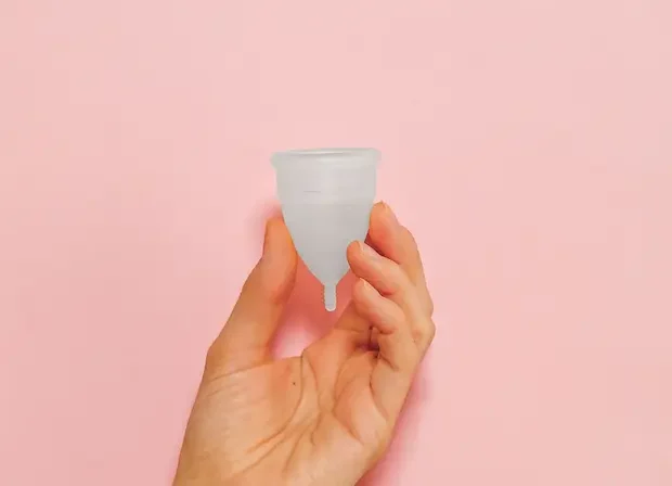 Une main tenant une tasse menstruelle rose sur un arrière-plan rose vif, soulignant la durabilité et la santé féminine.